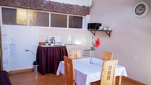 Un comedor acogedor con una mesa dispuesta para dos, una cocina al fondo y un reloj en la pared.