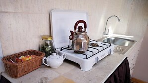Una cocina con estufa a gas, tetera, pileta y una cesta con objetos.