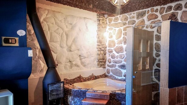 A stone-walled bathroom with a bathtub, a shower area, and a fireplace.