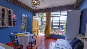 A room with a bed, a table with chairs, a window with curtains, and a fire extinguisher on the wall.