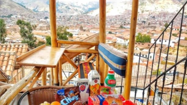 Un balcón con una silla y una mesa de mimbre, y una cesta de mimbre llena de frutas y aperitivos.