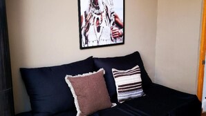 Un sofá azul oscuro con dos almohadones, un cuadro en la pared y una viga de madera en el techo.