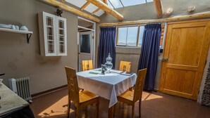 Un comedor con una mesa dispuesta para cuatro, sillas de madera, una ventana con cortinas y una puerta.