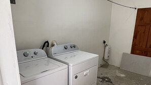 A laundry room with two white washing machines, a wooden door, and a concrete floor.