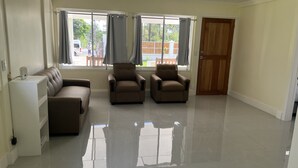 A spacious living room with a beige sofa, two armchairs, and a white cabinet.