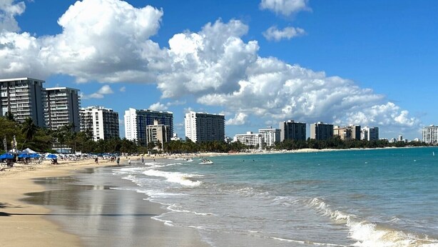 Una playa con cielos despejados, una orilla arenosa y edificios altos al fondo.