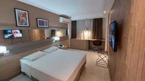 A hotel room with two beds, a desk, a chair, a TV, and artwork on the wall. - Mar Premier Flats (Queimados)