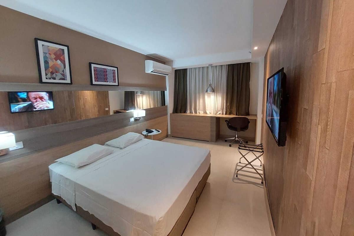 A hotel room with two beds, a desk, a chair, a TV, and artwork on the wall.