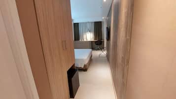 Un pasillo estrecho que conduce a un dormitorio con cama, escritorio y silla.
