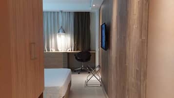 A narrow hallway leading to a bedroom with a bed, a desk, and a chair.