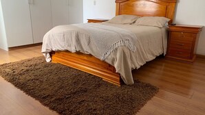 Ein Schlafzimmer mit einem hölzernen Bett, einem braunen Teppich, einem Nachttisch und einem Kleiderschrank.