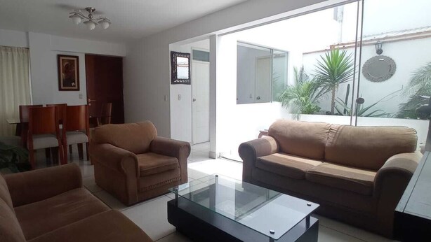 Ein Wohnzimmer mit Glastisch, zwei Sofas und einer Essecke mit Stühlen.