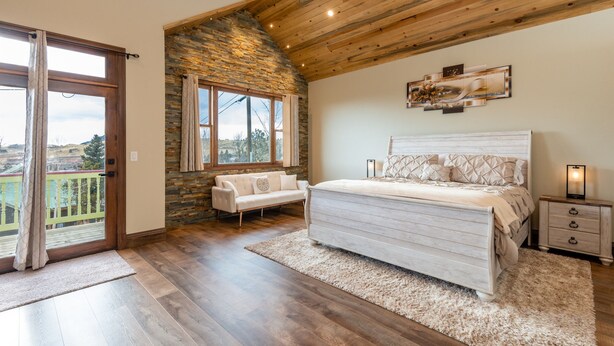 Une chambre avec un mur d’accent en pierre, un grand lit, une table de chevet et une vue sur un balcon accessible par une porte coulissante.
