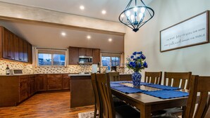 A modern kitchen with wooden cabinets, a central island, and a dining area with a table set for four. - Central A/C1895 Victorian*Hot Tub*MTN Views (Cripple Creek)
