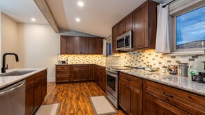 A kitchen with wooden cabinets, a stainless steel microwave, and a tiled backsplash. - Central A/C1895 Victorian*Hot Tub*MTN Views (Cripple Creek)