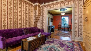 A room with a purple sofa, a wooden coffee table, and a patterned rug. There is a staircase leading to another room, and a dining area with a table and chairs. - Central A/C1895 Victorian*Hot Tub*MTN Views (Cripple Creek)