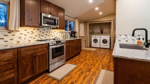A kitchen with wooden cabinets, a microwave, an oven, a washing machine, and a sink. - Central A/C1895 Victorian*Hot Tub*MTN Views (Cripple Creek)