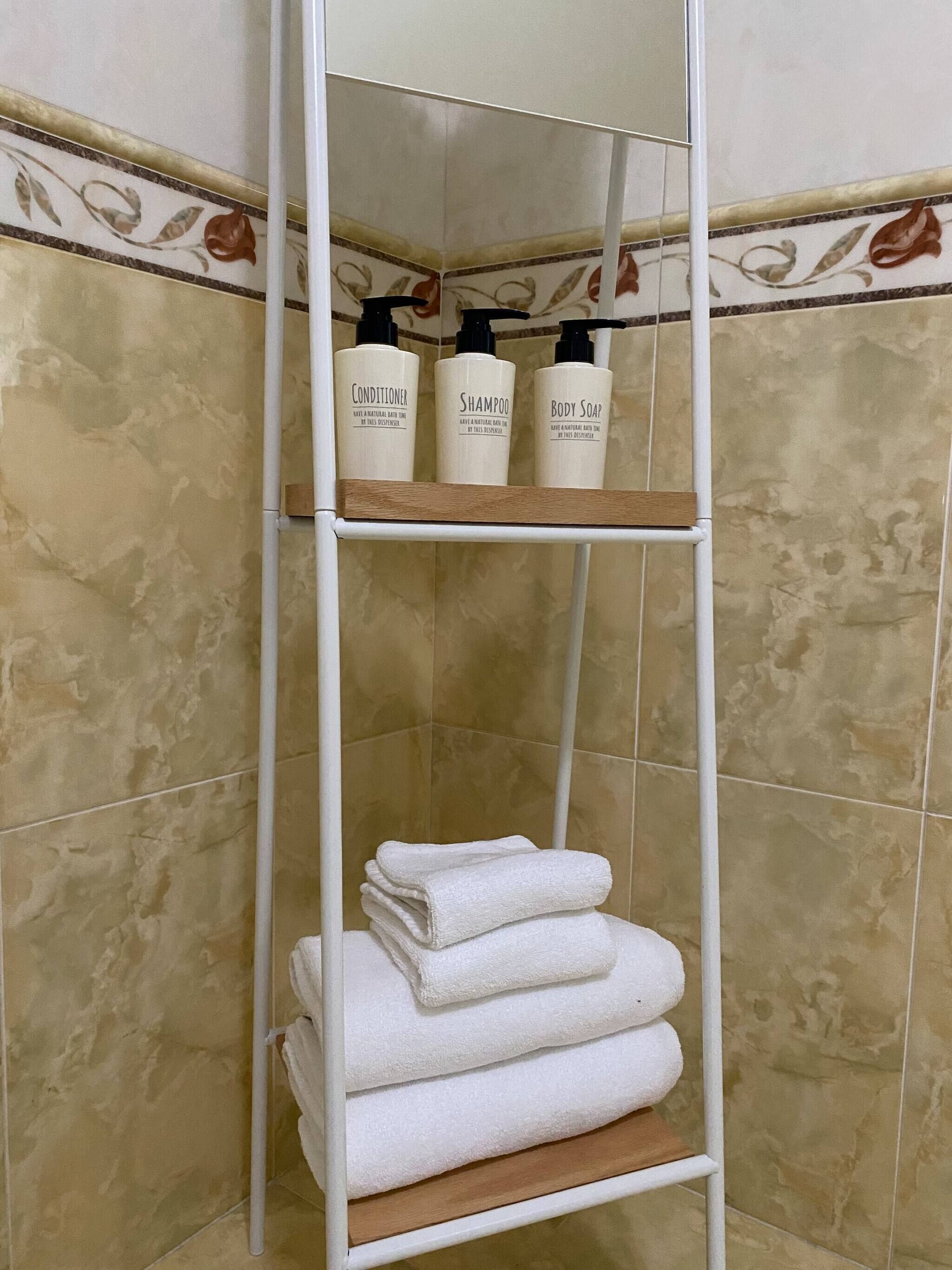 Une salle de bain avec une étagère en métal blanc où sont rangés les articles de toilette et les serviettes.