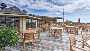 Une terrasse extérieure avec des tables et des chaises en bois, un espace salon couvert et une vue sur la mer.