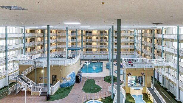 Un hôtel à plusieurs étages, avec des balcons, une piscine centrale et une salle de jeux.