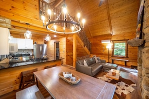 A wooden cabin interior with a dining area, kitchen, and living room.