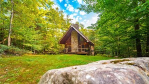 A rustic cabin with a stone facade, surrounded by dense forest and a clear sky. - Luxury ADK Retreat Near Whiteface, Lake Placid (Jay)