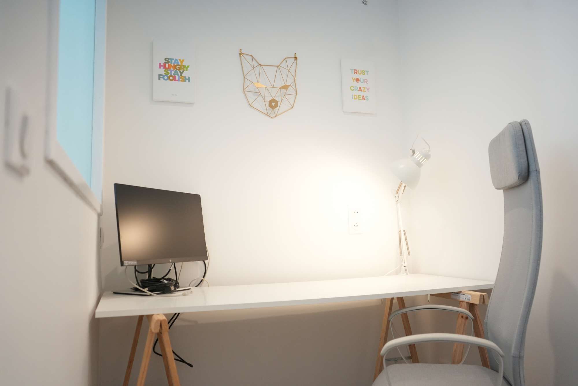 Un espace de bureau minimaliste comprenant un bureau, une chaise et une œuvre d’art accrochée au mur.
