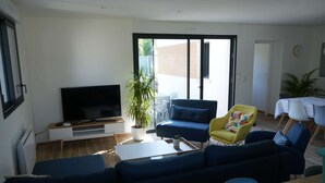 A modern living room with a large flat-screen TV, a blue sofa, a yellow armchair, and a dining area with a table and chairs. - Contemporary house at the gates of Brest (BOHARS)