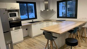 A modern kitchen with a wooden island, bar stools, and a stainless steel range. - Contemporary house at the gates of Brest (BOHARS)