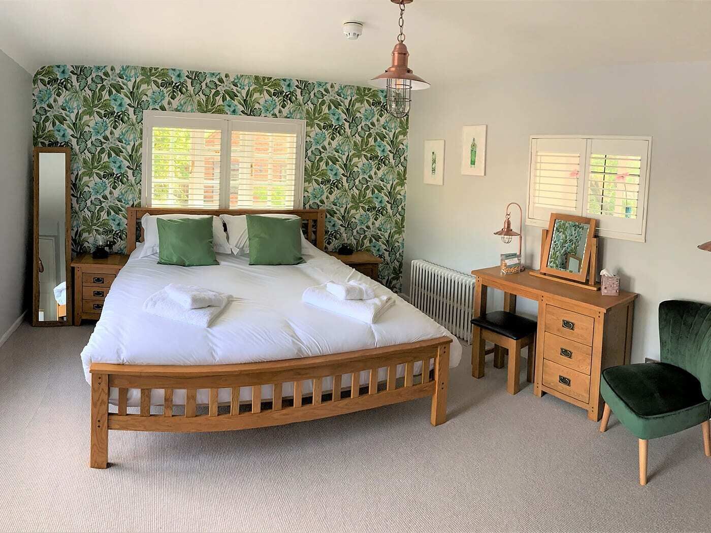 Un dormitorio con una cama de madera, almohadas verdes, un aparador de madera, una silla verde y un radiador.