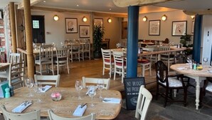 Un restaurante con varias mesas y sillas, vigas de madera en el techo y cuadros en las paredes.