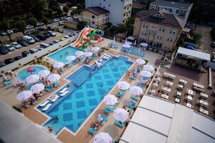 Un área de piscina en la azotea con varias piscinas, sillas de descanso, sombrillas y un tobogán de agua.