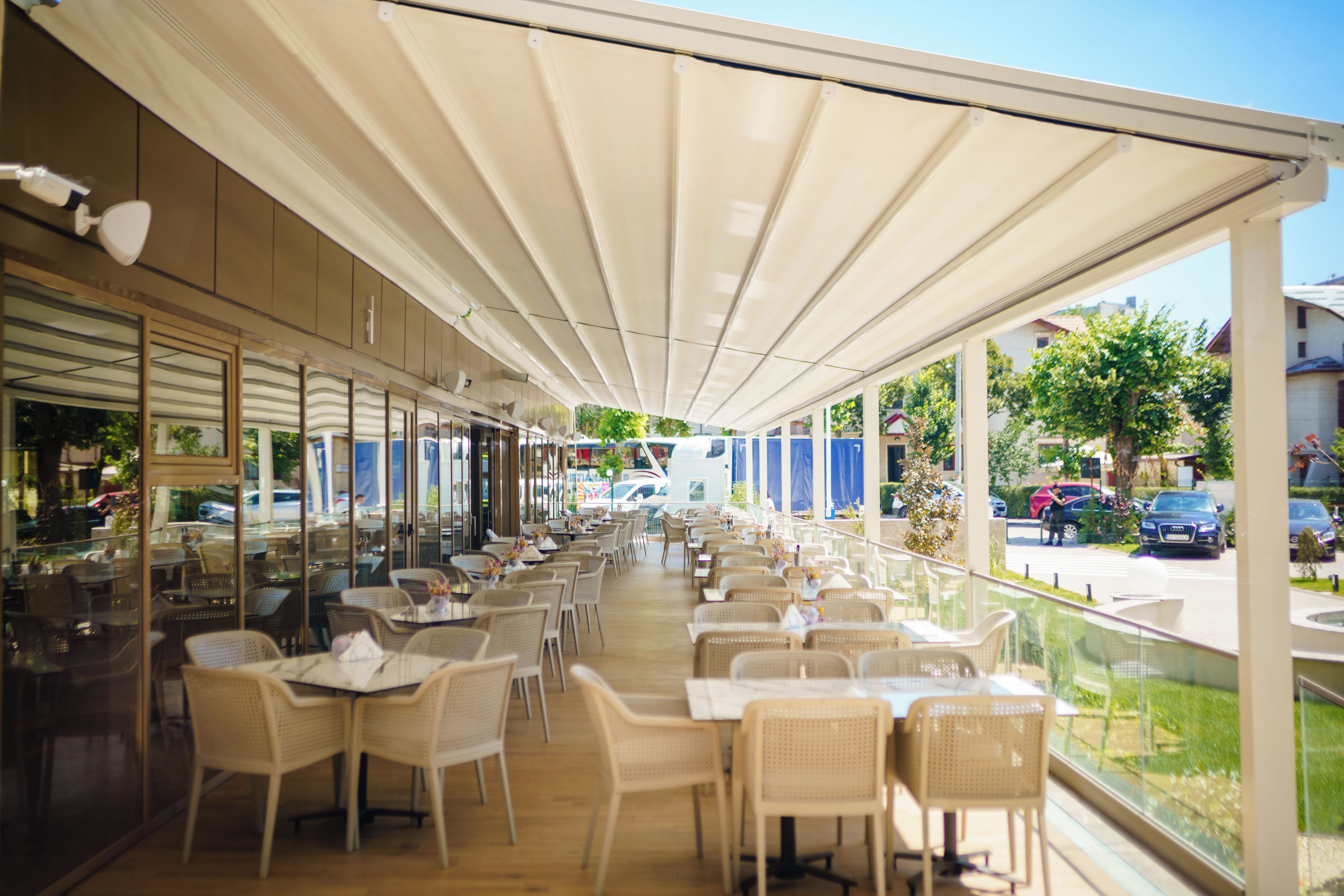 An outdoor cafe with tables and chairs, a covered walkway, and a view of the street.
