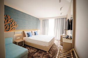 A hotel room with a bed, a desk with a telephone, a chair, and a large artwork on the wall.