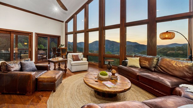 A spacious living room with leather sofas, a round coffee table, and a view of mountains through large windows. - 14 Acres - Theater Room - 20 Miles to DT Asheville - Paved Drive the whole way! (Canton)