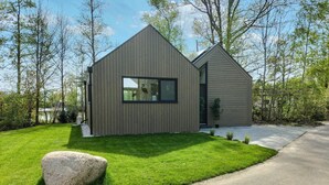 A modern two-story house with a sloped roof, a large window on the front, and a well-maintained lawn.