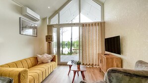A modern living room with a sofa, a coffee table, a TV, and a large window with curtains.