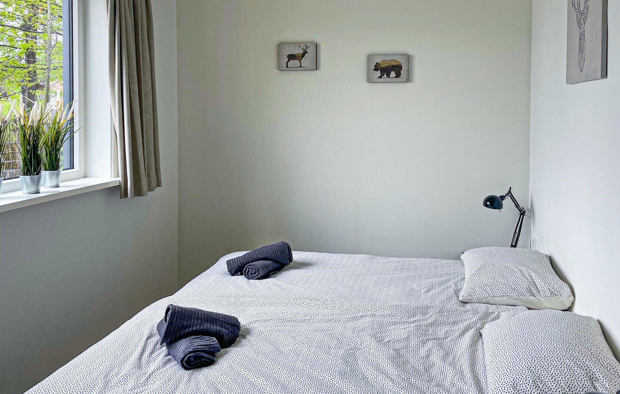 Une chambre à coucher avec un lit, deux oreillers, une lampe et deux œuvres d’art murales représentant un cerf et un ours.