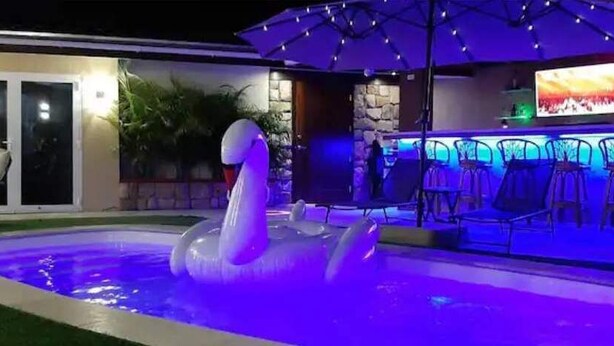 A swimming pool with a swan float, a bar area with chairs, and a television screen. - Arupar Apartment (PARADERA)