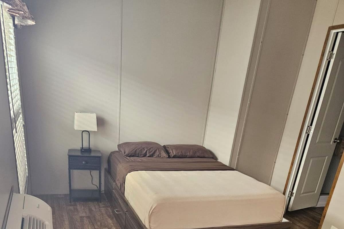 A bedroom with a bed, a nightstand, a lamp, and a heater.