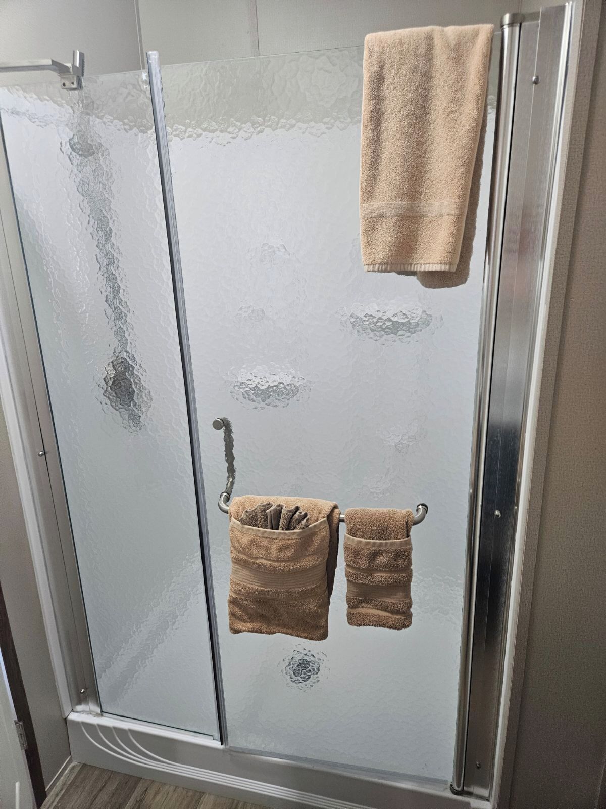 A glass shower enclosure with two towels hanging on a rack.