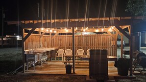 Una estructura de madera al aire libre con una zona de bar, asientos y una parrilla.