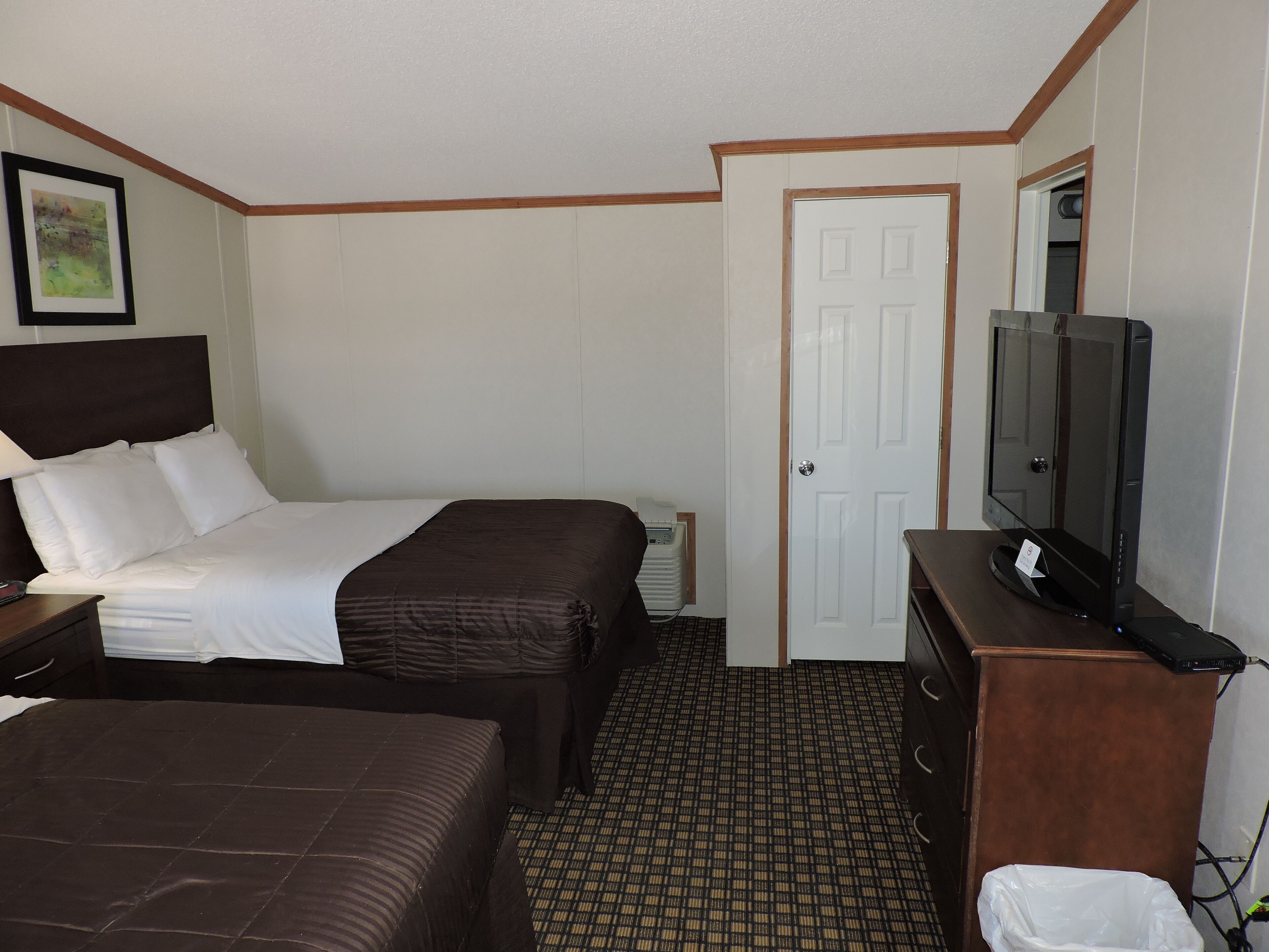 Une chambre d’hôtel avec deux lits, une télévision, une commode et une porte.