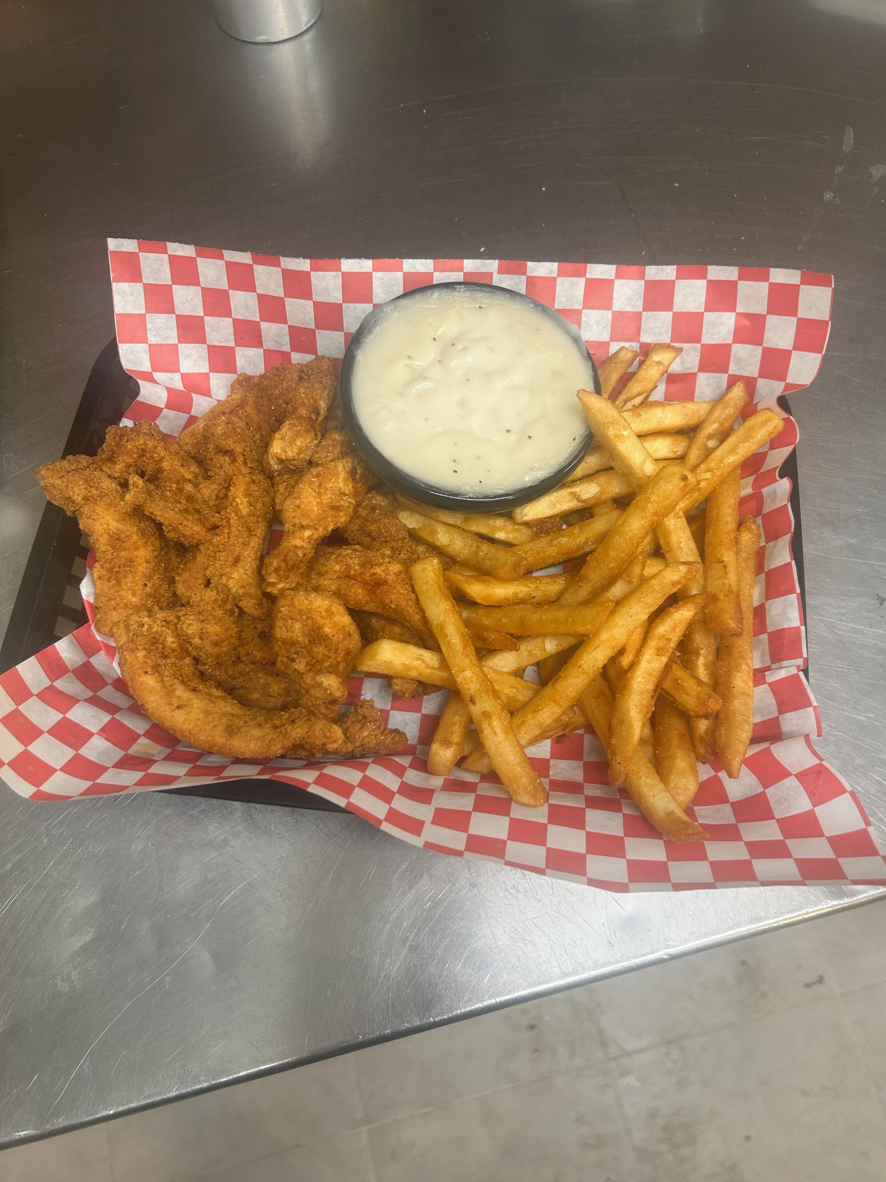 Un vassoio con pollo fritto e patatine fritte su carta a scacchi.