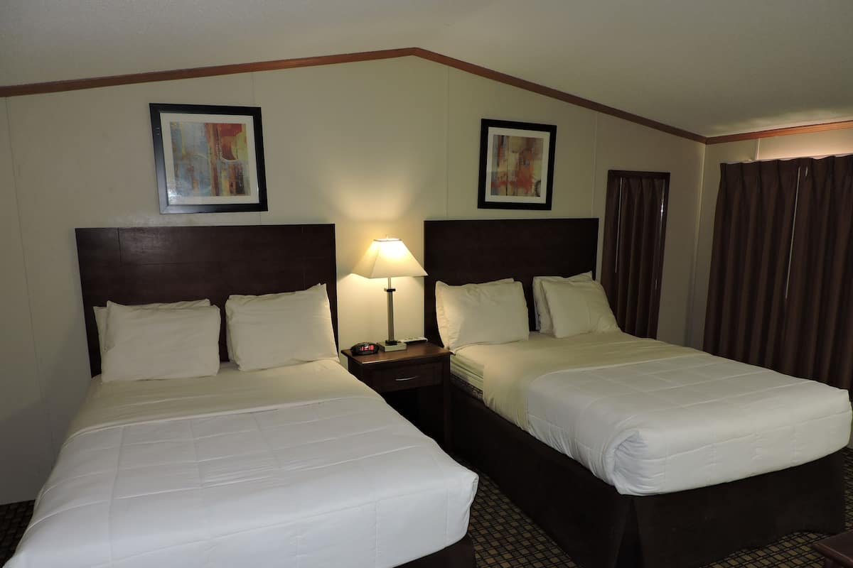 A hotel room with two beds, a nightstand with a lamp, and two framed pictures on the wall.