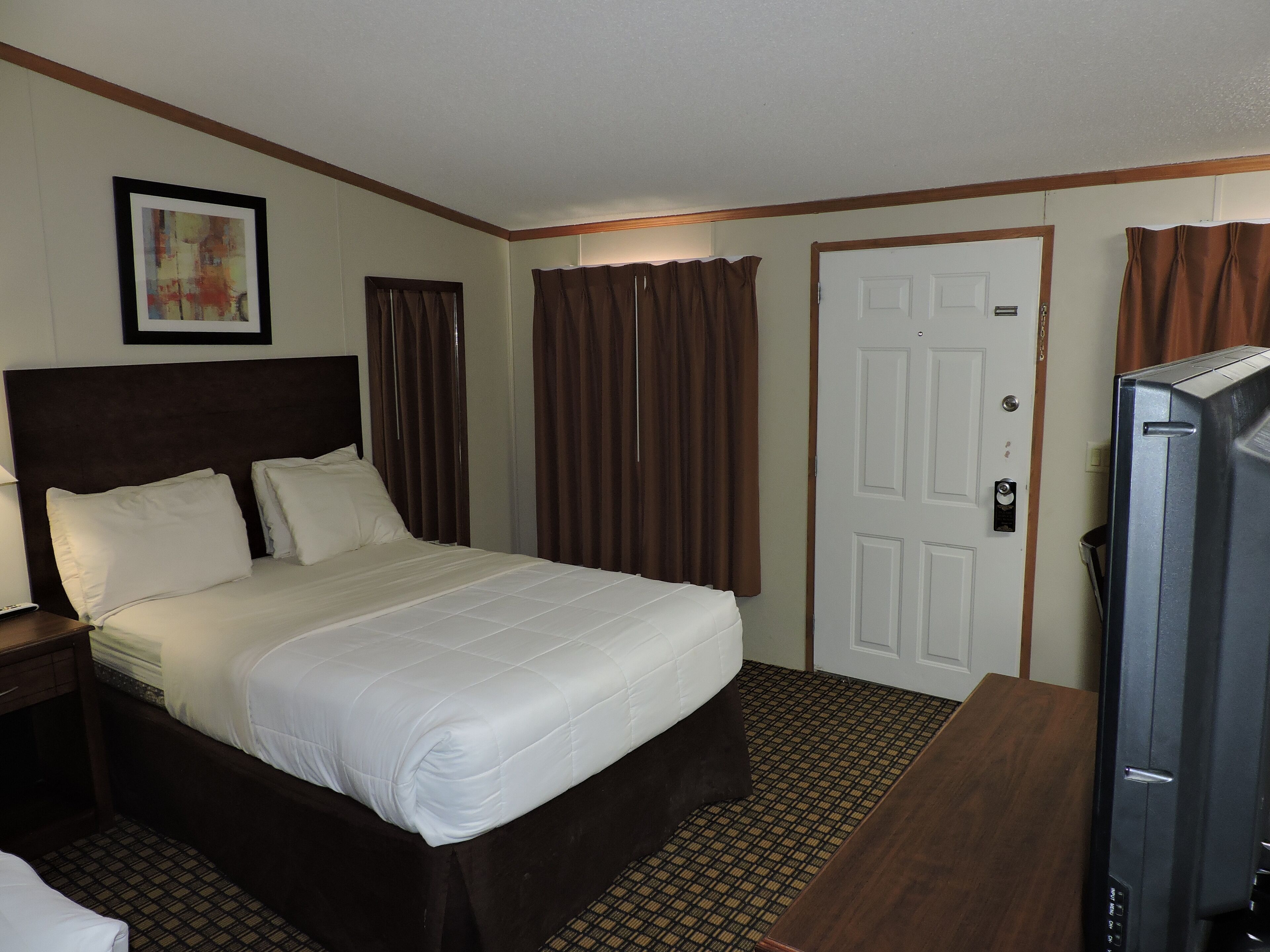 A hotel room with a bed, a television, a door, and a window with curtains.
