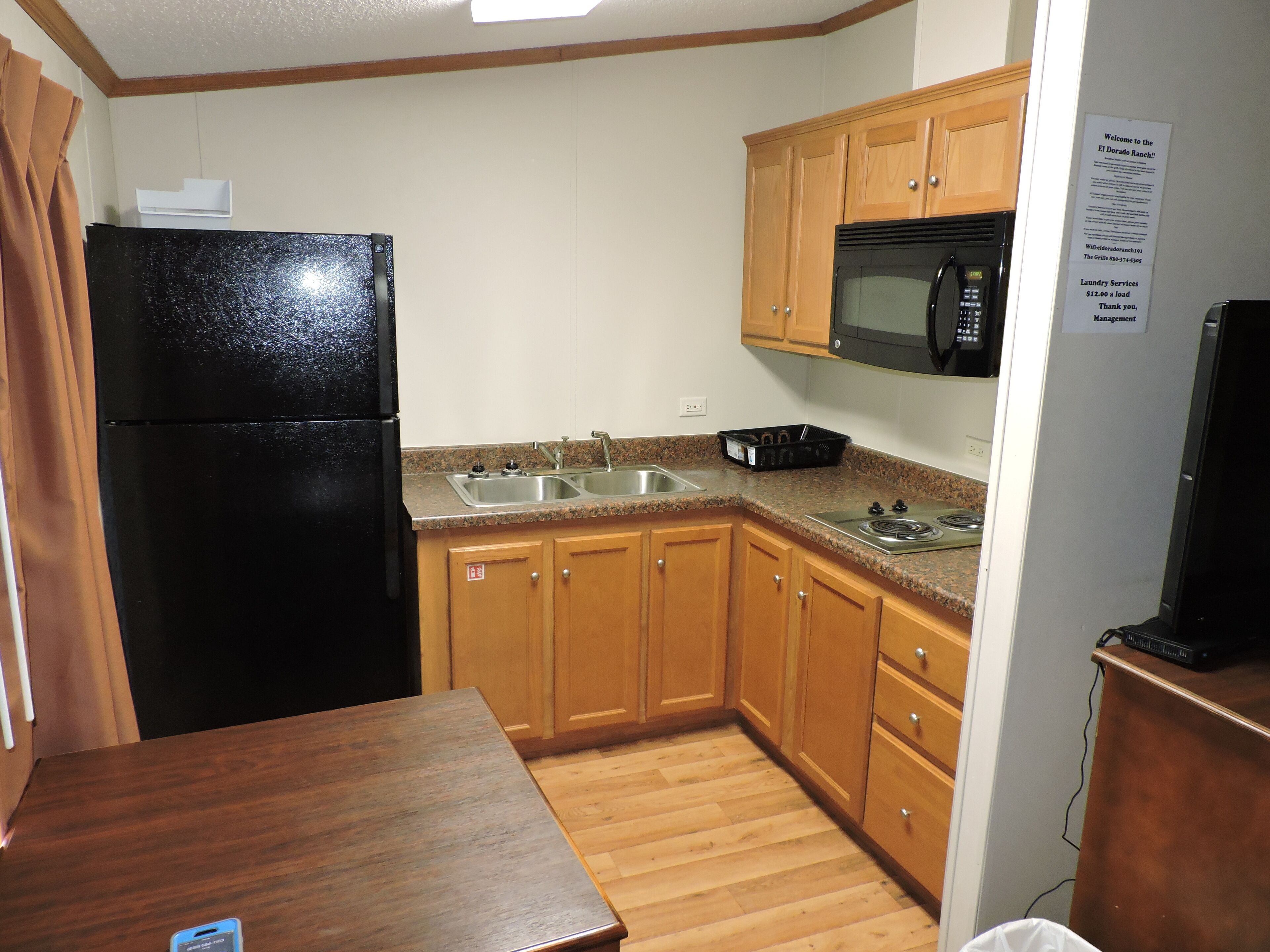 A compact kitchen with wooden cabinets, a black refrigerator, a stainless steel sink, and a microwave.