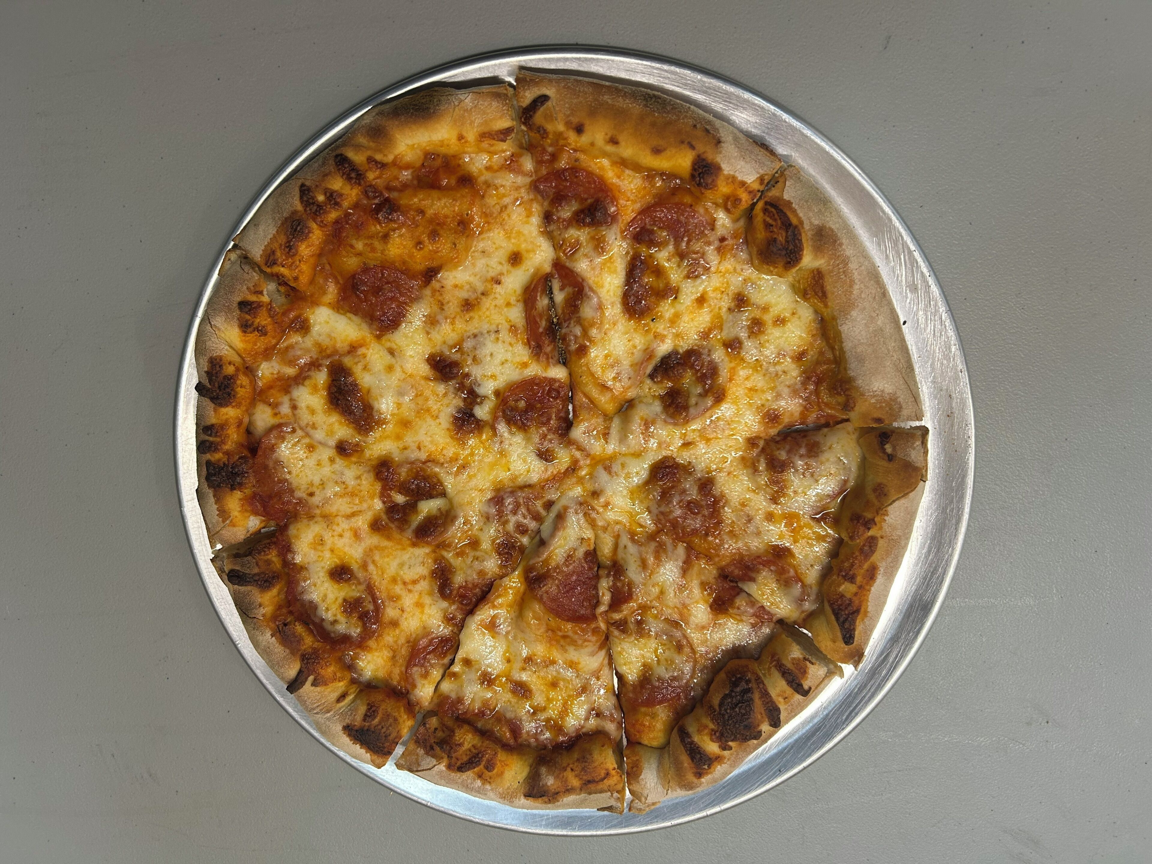 A pizza with pepperoni and cheese on a round metal tray.