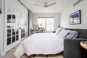 A bedroom with a bed, a gray sofa, a desk with a chair, a window, and a ceiling fan. - Beautiful Luxury Home located at Island Pointe Marina!
Just 1 mile to downtown! (St. Joseph)