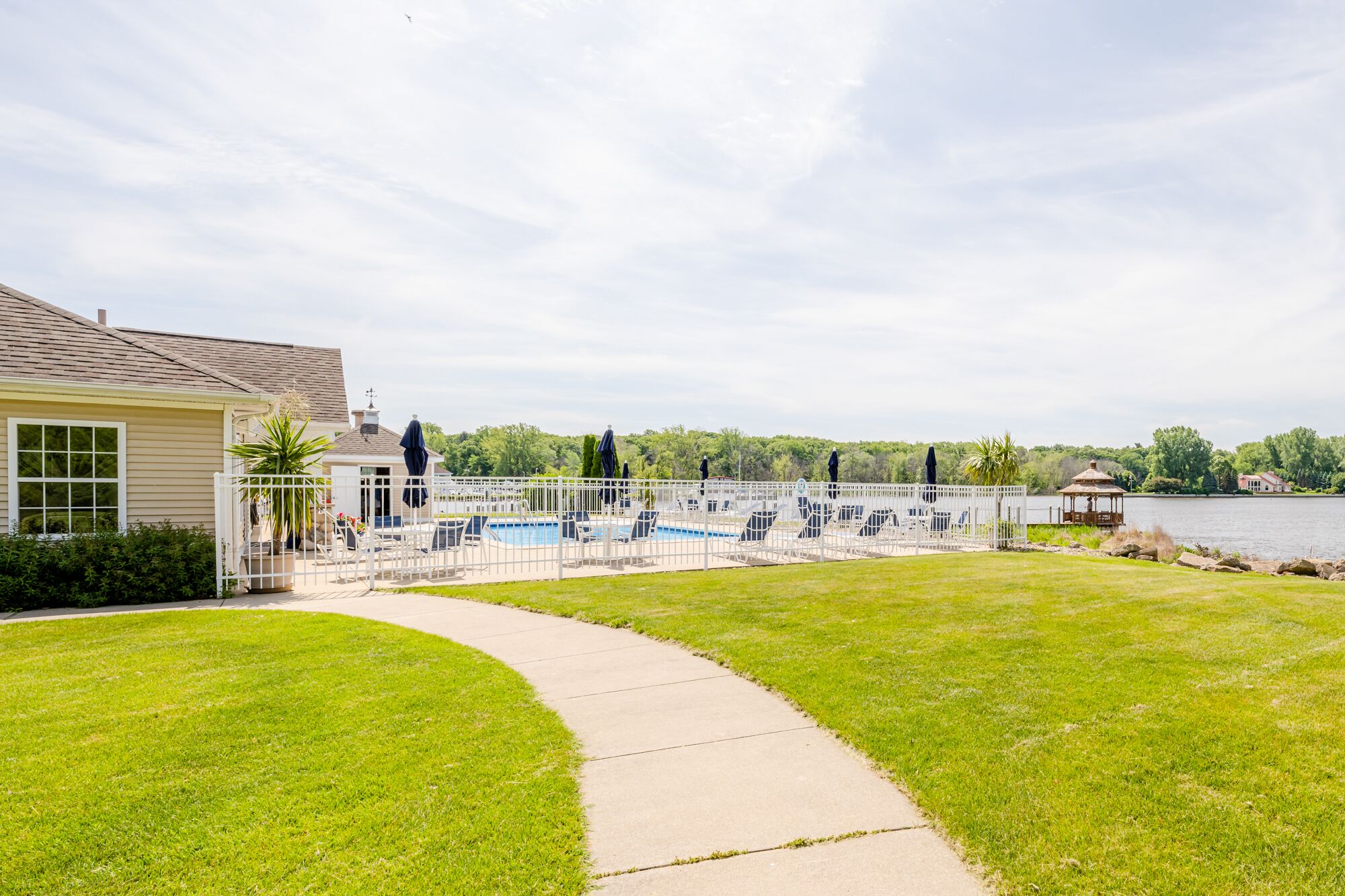 A pool area with lounge chairs and a gazebo, surrounded by a white fence and a pathway.